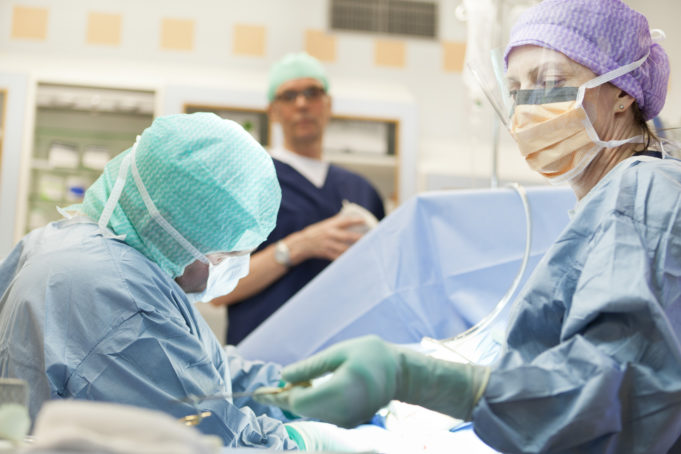 Kolme suoja-asuista ammattilaista suorittavat kirurgista toimenpidettä potilaalle.