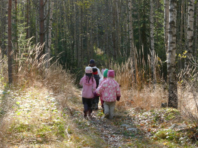 Lapsia kävelee käsi kädessä metsäpolulla.
