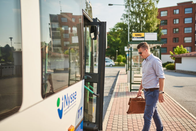 Mies astumassa Nyssen bussiin bussipysäkillä. Mies on työmatkalla kädessään salkku.