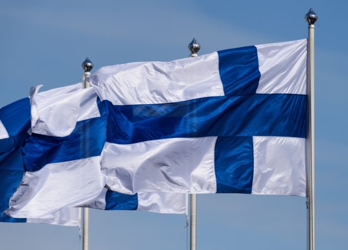 Kaksi Suomen siniristilippua liehuu aurinkoisessa säässä vierekkäisissä lipputangoissa.