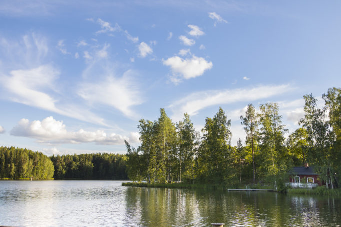 Järvinäkymä, jossa rannalla näkyy puita sekä punainen puurakennus.