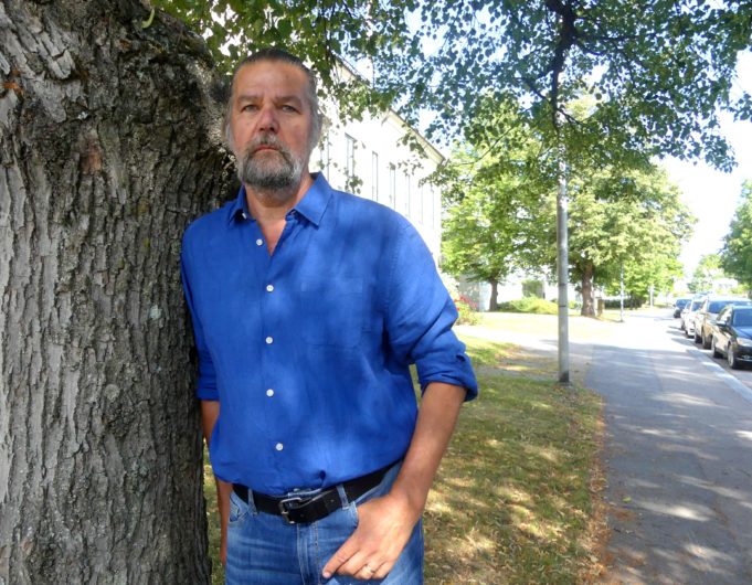 Toimittaja Matti Kuusela nojaa puuhun kaupungintalon edustalla.