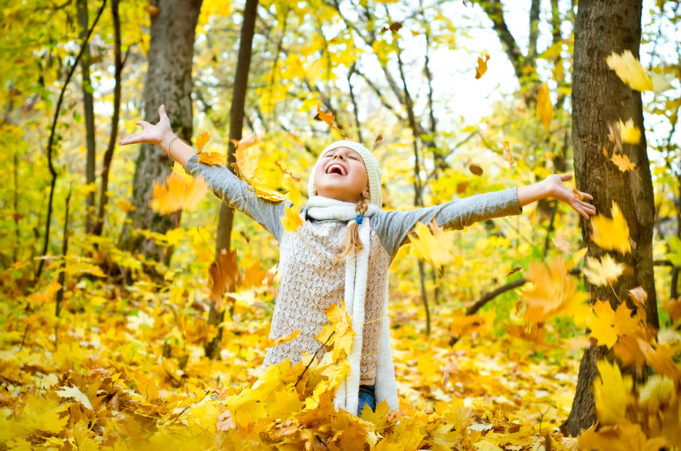 Nuori tyttö heittää keltaisia vaahteranlehtiä ilmaan puistossa syksyllä.