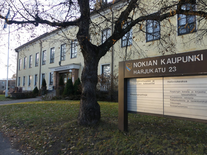 Nokian keltainen kaupungintalo, edustalla Nokian kaupungin kyltti ja lehdetön puu.