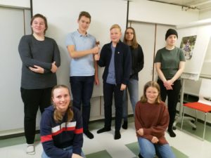 Nuorisovalstuuston jäsenet yhteiskuvassa. Kuvassa seitsemän nuorta, joista viisi seisoo takana ja kaksi kyykyssä edessä. Puheenjohtajat seisovat keskellä takana ja pitävät yhteisesti käsissä nuijaa.