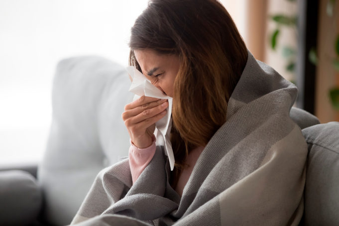 Flunssaan sairastunut nainen istuu sohvalla ja niistää nenäliinaan.