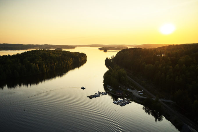 Siuron satama kesäiltana auringon laskiessa järven taakse. Satamalaiturissa on veneitä kiinnitettynä ja yksi moottorivene on suuntaamassa takaisin satamaan.