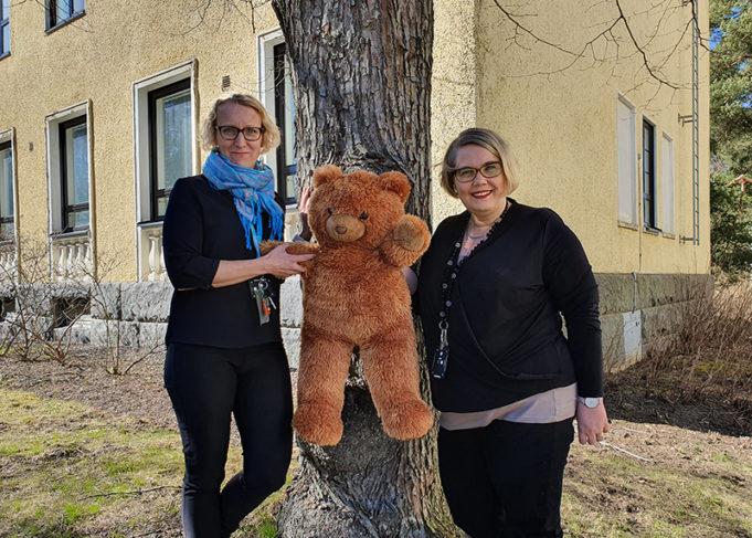 Johtavat sosiaalityöntekijät ja nalle kuvattuna puun edessä.
