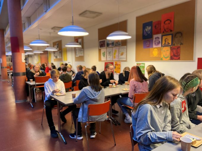 Oppilaita istuu ruokalassa syömässä glögiä ja leivoksia.