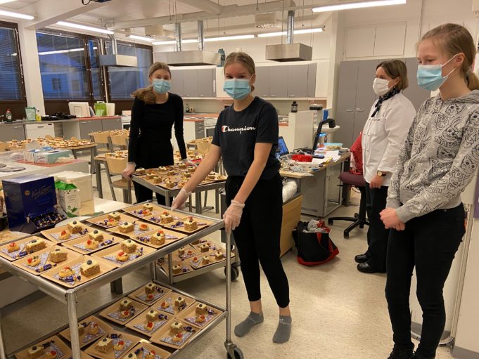 Tyttöjä seisoo kotitalousluokassa kasvomaskit kasvoilla ja siirtelee kärryissä leivoksia.