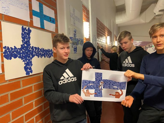 Kaksi poikaa pitelee paperista Suomen lippua. Muita oppilaita on takana koulun käytävällä