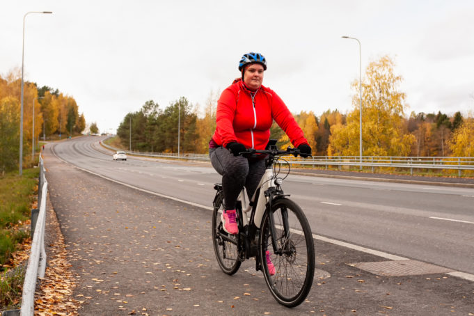 Punaiseen tuulitakkiin pukeutunut nainen polkee sähköpyörällä Nokianvaltatietä pitkin syksyllä.