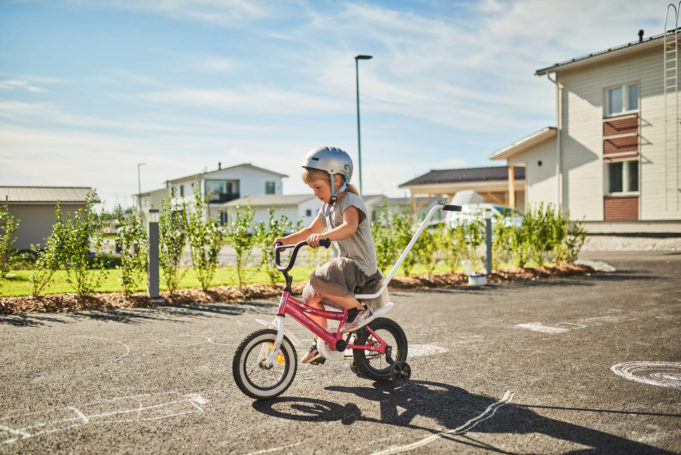Pieni tyttö ajaa polkupyörällä omakotitalon asfaltoidulla pihalla.