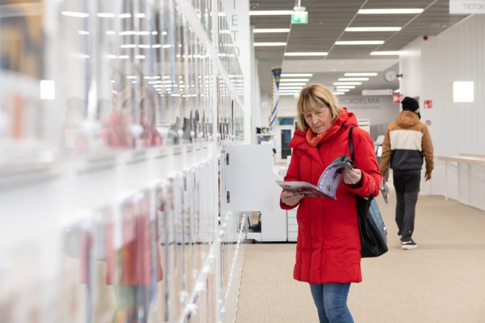 Punaiseen takkiin pukeutuntu nainen selailee aikakauslehteä kirjasto- ja kulttuuritalo Virrassa.