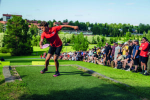 Frisbeegolfheitto lähdössä kilpailijalla nokian kentällä. Yleisöä seuraamassa tapahtumaa.