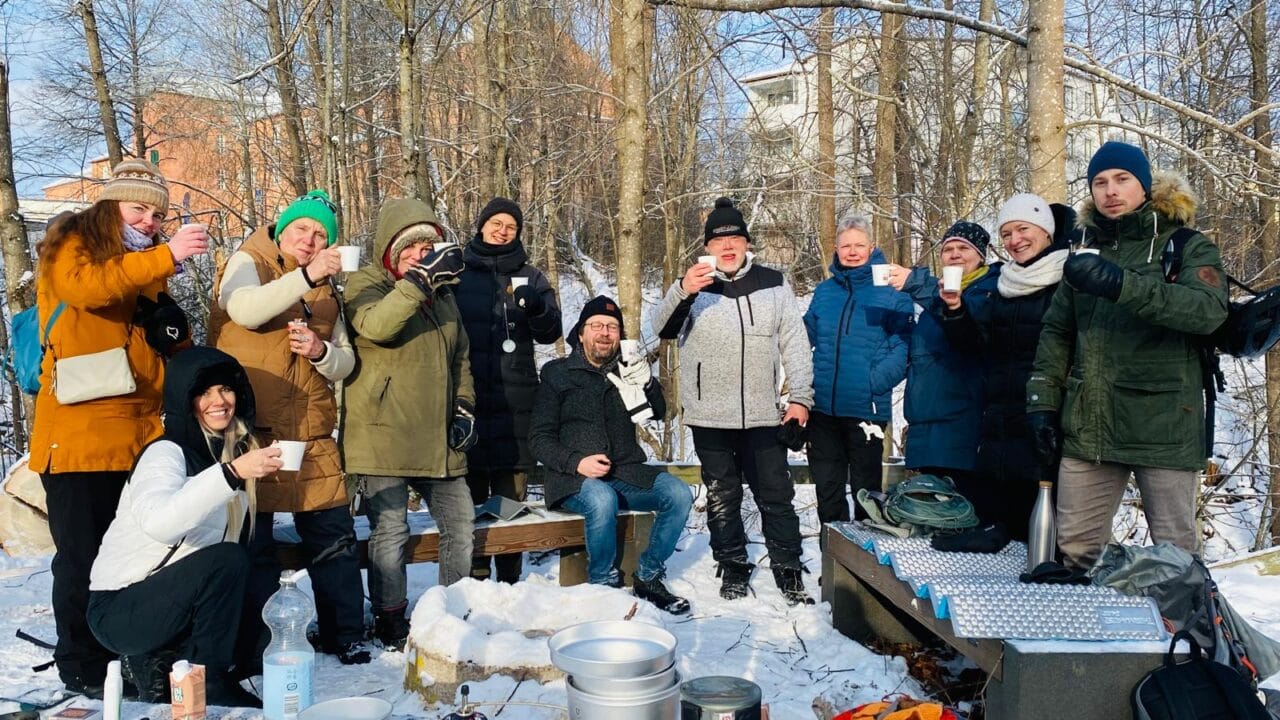 Iloisia ihmisiä talvisessa luonnossa kahvimukit kädessä